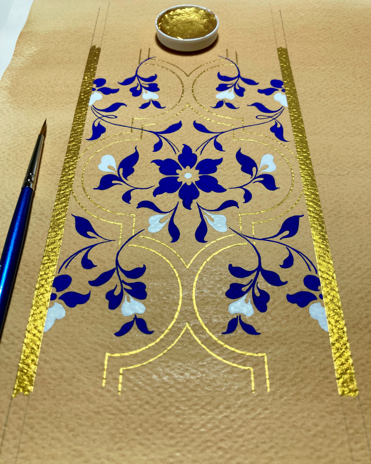 Decorative floral design by Charlotte Dilley with blue flowers on a gold background, using a paintbrush and container of gold paint.