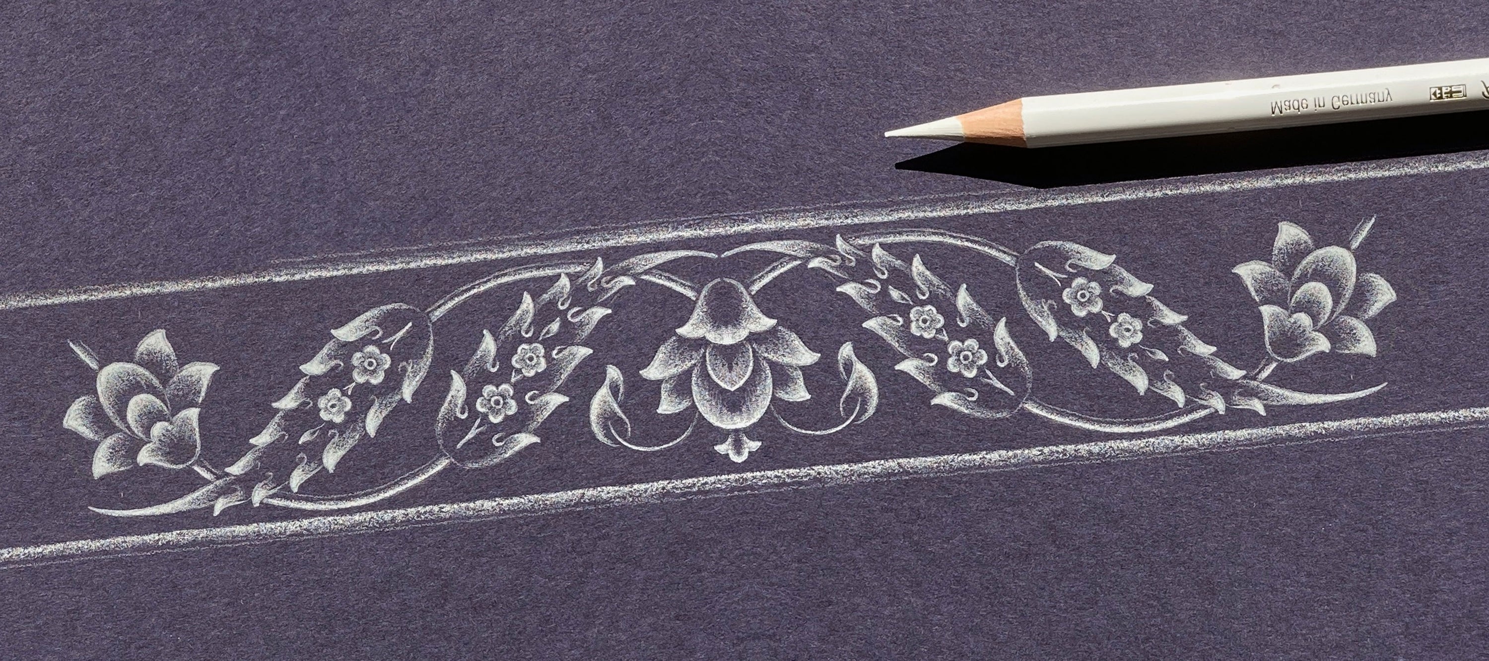 Decorative floral design on a dark surface with a pencil.