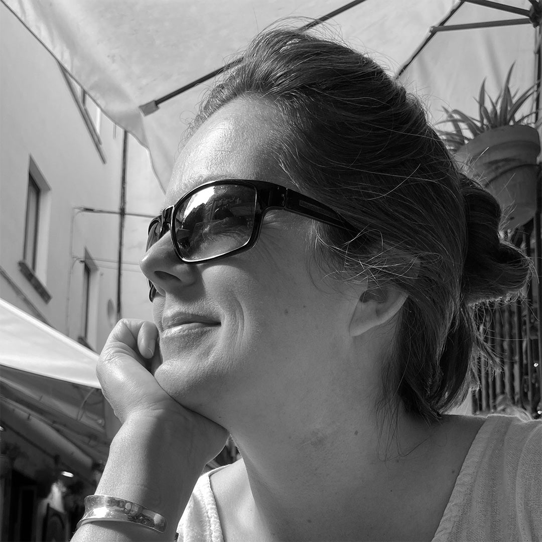 A black and white close-up portrait of artist Charlotte Dilley, resting her chin on her hand in an outdoor setting in Seville, Spain.