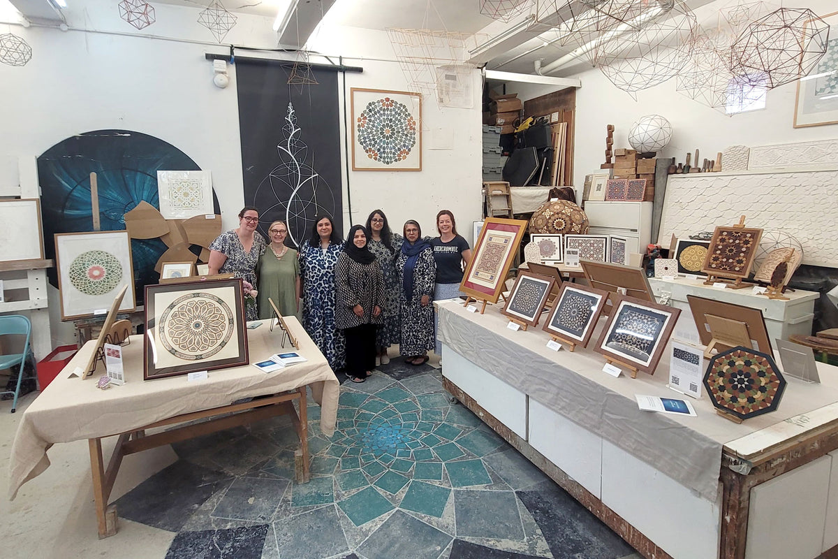 Group of artists in London studio with framed biomorphic and geometric artwork on tables and walls.