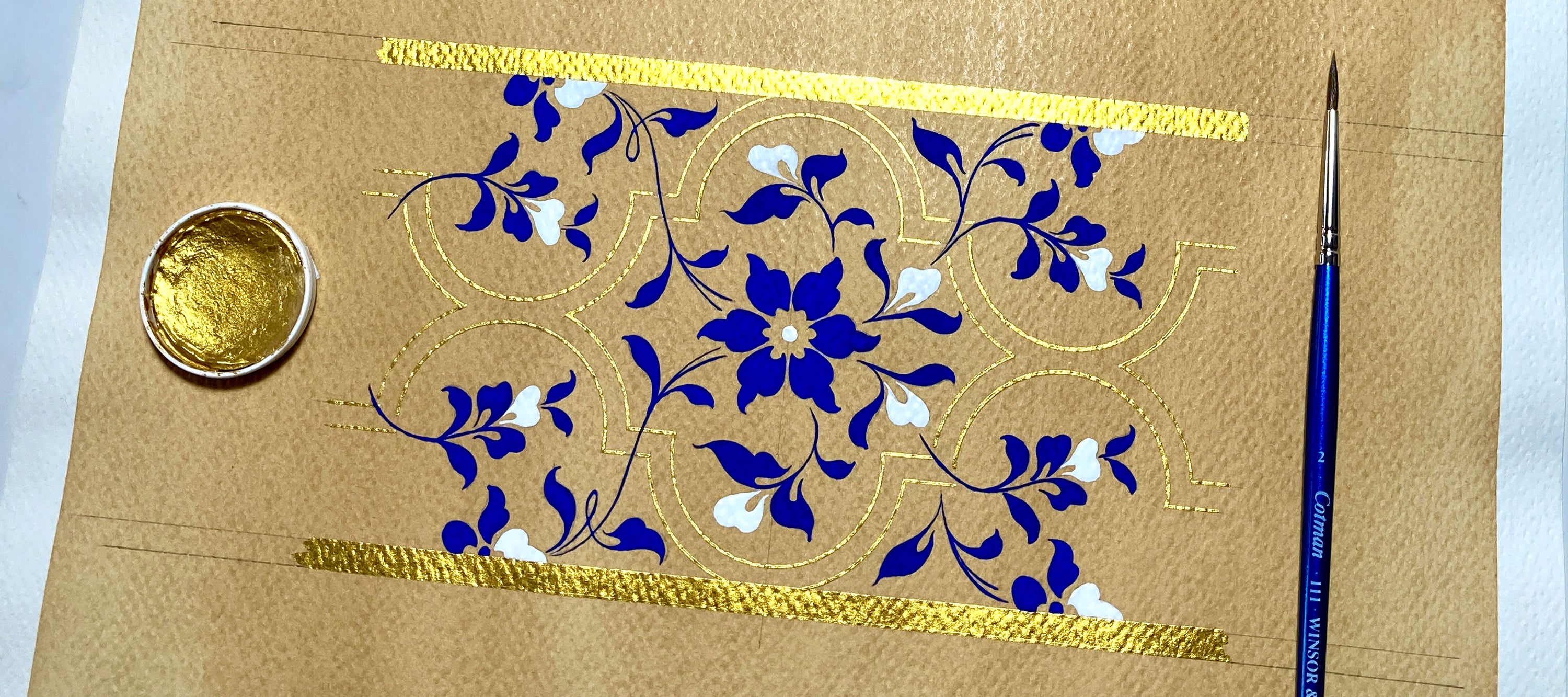 Decorative painting by Charlotte Dilley with blue floral design, gold accents, and a brush on a white background