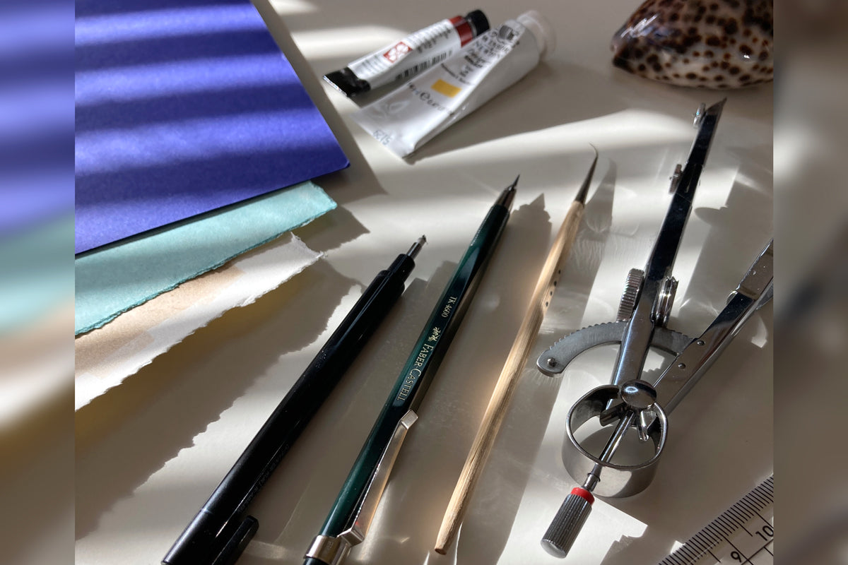Art tools and materials including pens, pencils, and a ruler in dappled sunlight.