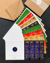 Flat lay of 8 square christmas cards in green, red, blue and yellow ornamental pattern and kraft envelopes